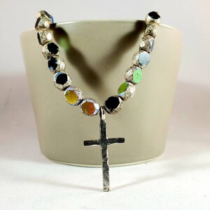 May include: A silver cross pendant necklace with a beaded chain. The beads are iridescent and have a variety of colors, including black, green, yellow, and orange.