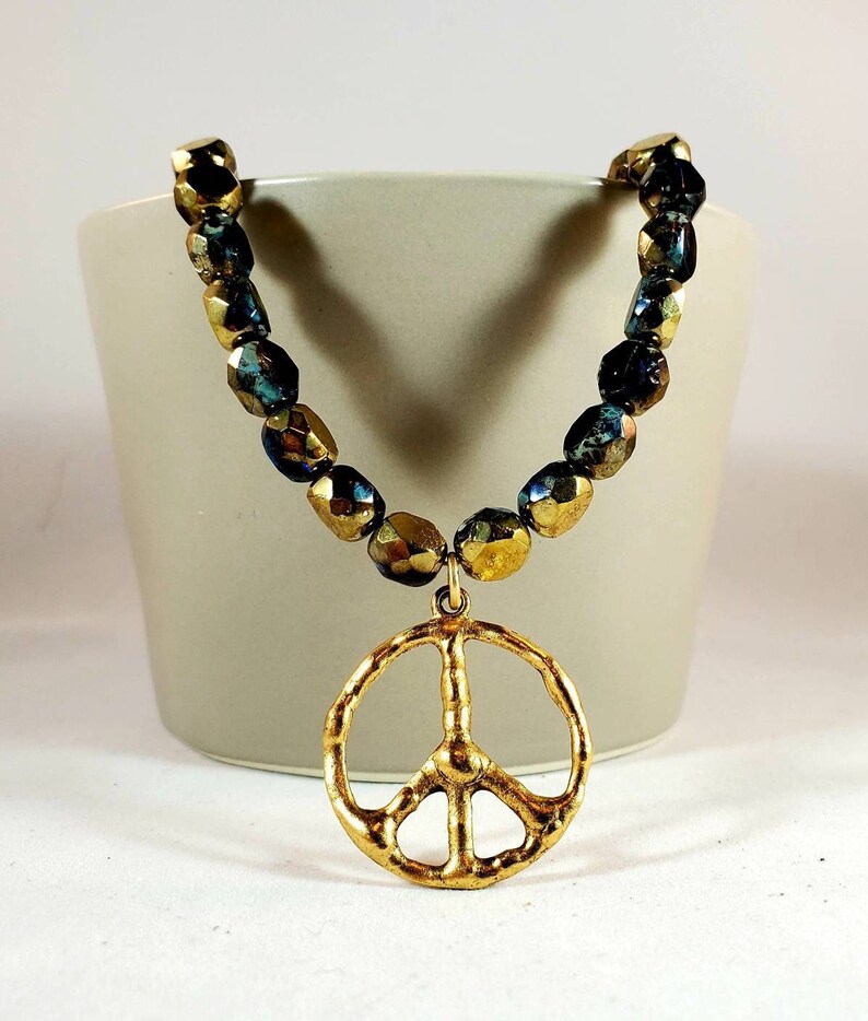 May include: A gold peace sign pendant necklace with a beaded chain made of iridescent blue and gold glass beads.