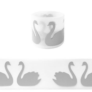 May include: A white candle with a silver swan design. The candle is in a cylindrical container and has a silver swan design on the side. The candle is surrounded by a white background.