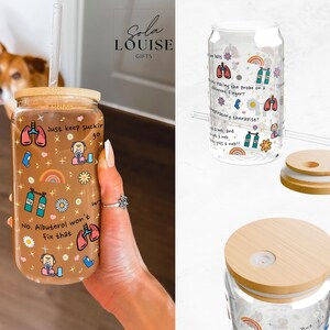 May include: A clear glass reusable tumbler with a straw and a lid. The tumbler has a colorful design with illustrations of lungs, oxygen tanks, and the text "Just keep suckin'" and "No. Albuterol won't fix that".