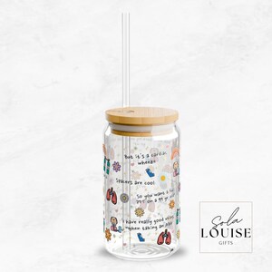 May include: A clear glass reusable water bottle with a bamboo lid and a straw. The bottle is decorated with colorful stickers and text that says "But it's a cute-a-whoops" and "Spikes are cool".