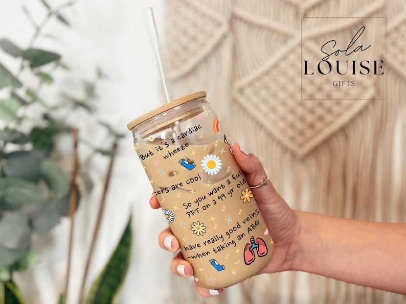 May include: A clear glass tumbler with a bamboo lid and a straw. The tumbler is decorated with colorful drawings of flowers, hearts, and medical symbols. The text on the tumbler reads "But it's a cardiac wheeze", "cers are cool", "So you want a full PFT on a 99 yr old", "have really good veins -when taking an ABG".