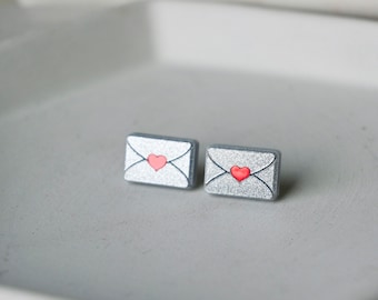 May include: A pair of silver earrings shaped like envelopes with a red heart on each.
