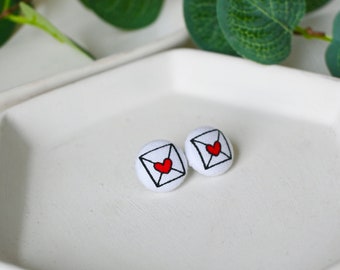 May include: A pair of white fabric earrings with a red heart inside a black outline of an envelope.