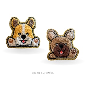 May include: Two embroidered iron-on patches featuring cartoon dogs. The first patch is a yellow and white corgi with a brown nose and a pink tongue. The second patch is a brown and white french bulldog with a brown nose and a pink tongue. Both patches have a gold glitter outline.