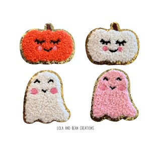 May include: Four Halloween-themed felt patches with gold glitter trim. Two patches are pumpkins with smiling faces and closed eyes. One pumpkin is orange and the other is white. The other two patches are ghosts with smiling faces and closed eyes. One ghost is white and the other is pink.