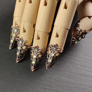 May include: Five ornate, pointed, metal finger rings with clear rhinestones. The rings are worn on a wooden hand model.