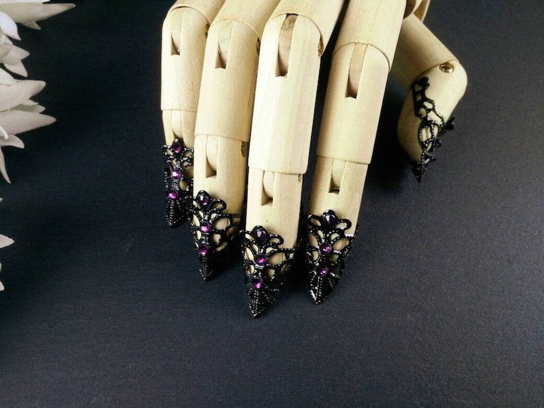 Puede incluir: Cuatro anillos de encaje negro para la punta de los dedos con piedras de imitaci&oacute;n de color p&uacute;rpura en un maniqu&iacute; de mano de madera.