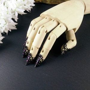 Puede incluir: Un maniqu&iacute; de mano de madera que lleva anillos de encaje negro para la punta de los dedos con diamantes de imitaci&oacute;n morados. Los anillos son puntiagudos y tienen un estilo g&oacute;tico.