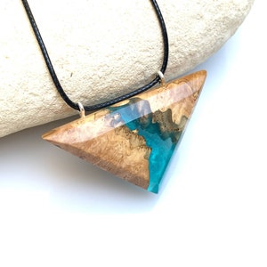 Op de afbeelding: Een ketting met een driehoekige hanger van hout en turquoise hars. De hanger is bevestigd aan een zwart koord.