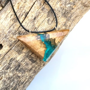 Op de afbeelding: Een driehoekige hangerketting met een ontwerp van hout en hars. De hars is een levendige turquoise blauwe kleur en het hout is een lichtbruine kleur. De ketting is aan een zwart koord.