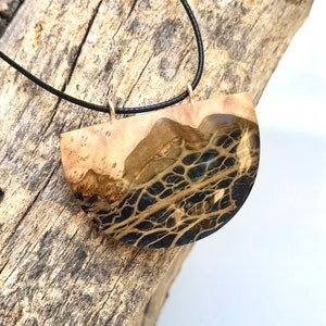 May include: A black cord necklace with a wooden pendant. The pendant is a half-circle shape with a dark brown and black marbled pattern.