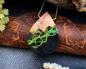 May include: A teardrop-shaped pendant necklace with a wood and resin design. The resin is black and green and features a lace-like pattern. The pendant is hanging from a silver chain.
