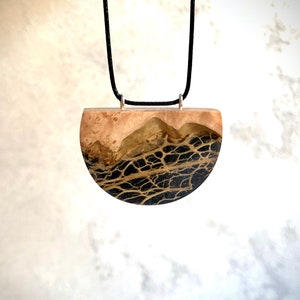 May include: A black and gold resin pendant necklace with a half-circle shape. The pendant features a unique design of black veins against a gold background.