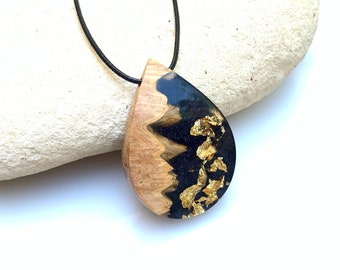 May include: A teardrop-shaped pendant necklace with a black resin and wood inlay. The resin is embedded with gold leaf flakes. The necklace is on a black cord.