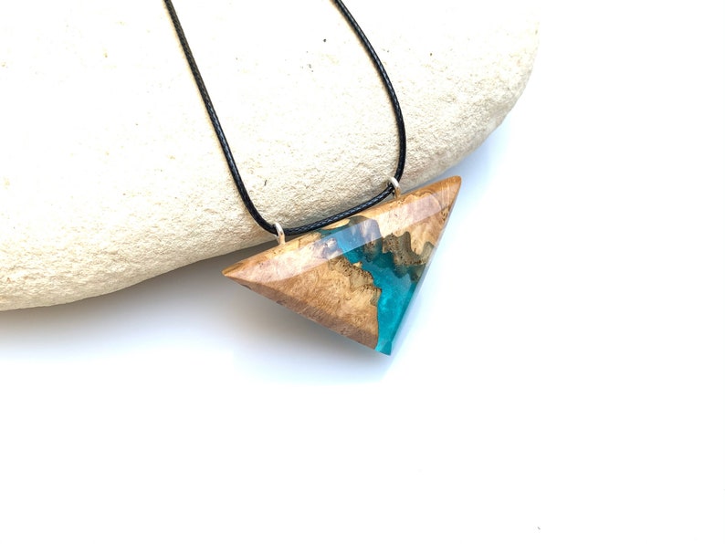 Op de afbeelding: Een ketting met een driehoekige hanger van hout en turquoise hars. De hanger is bevestigd aan een zwart koord.