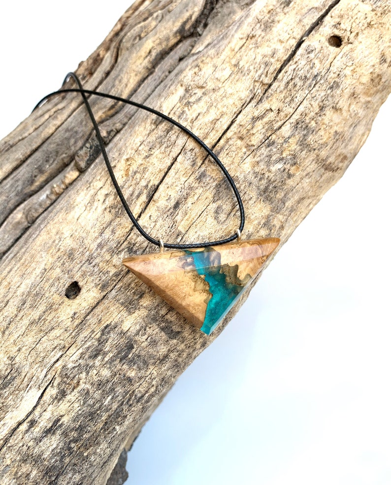 Op de afbeelding: Een driehoekige hangerketting met een ontwerp van hout en hars. De hars is een levendige turquoise blauwe kleur en het hout is een lichtbruine kleur. De ketting is aan een zwart koord.