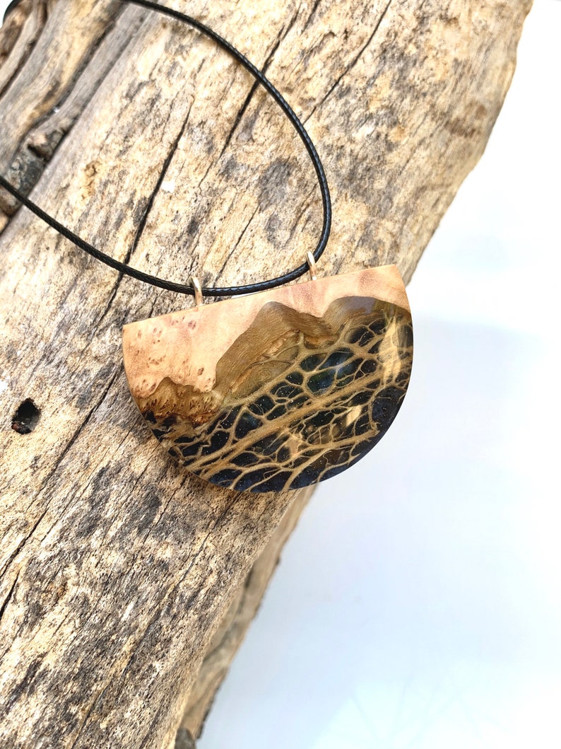 May include: A black cord necklace with a wooden pendant. The pendant is a half-circle shape with a dark brown and black marbled pattern.