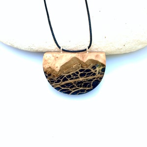 May include: A black and brown resin pendant necklace with a half-circle shape. The pendant has a natural wood look with black resin veins.