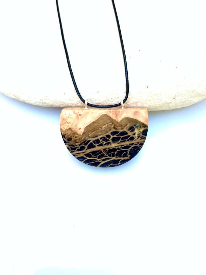 May include: A black and brown resin pendant necklace with a half-circle shape. The pendant has a natural wood look with black resin veins.