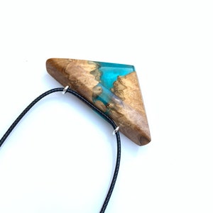 Op de afbeelding: Een driehoekige houten hanger met een turquoise harsinleg, hangend aan een zwart koord.