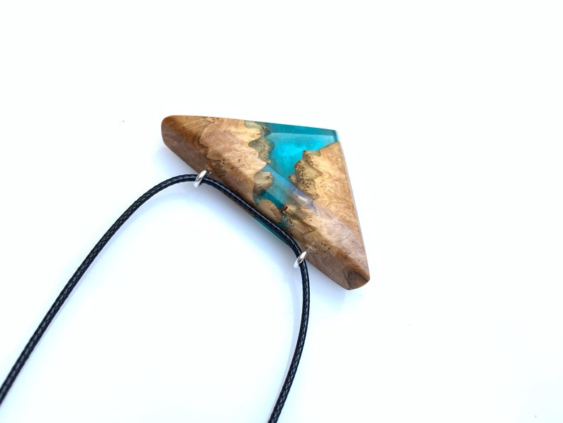 Op de afbeelding: Een driehoekige houten hanger met een turquoise harsinleg, hangend aan een zwart koord.