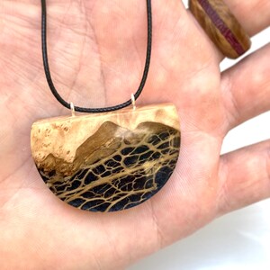 May include: A black cord necklace with a half-circle pendant made of wood and resin. The pendant has a black and gold marbled pattern.