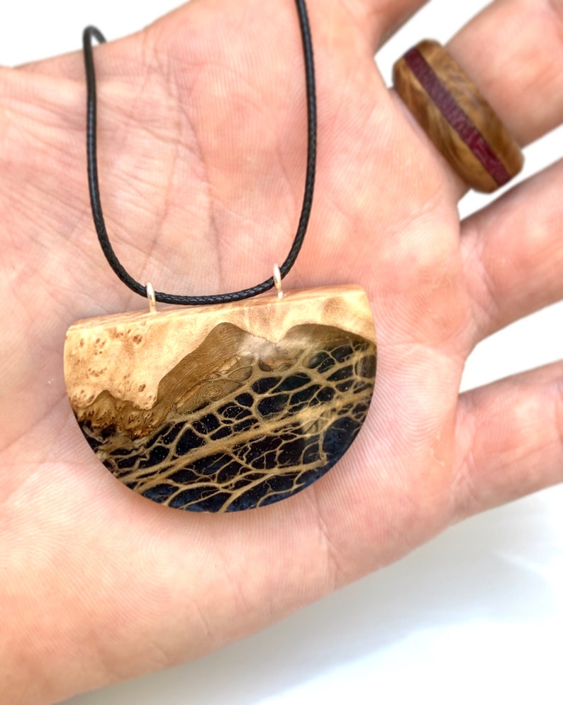 May include: A black cord necklace with a half-circle pendant made of wood and resin. The pendant has a black and gold marbled pattern.