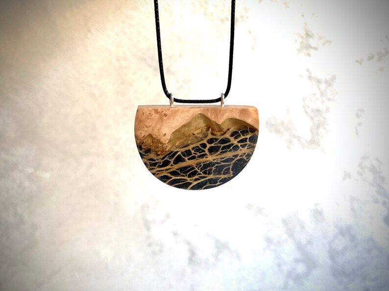 May include: A black and gold resin pendant necklace with a half-circle shape. The pendant features a unique design of black veins against a gold background.