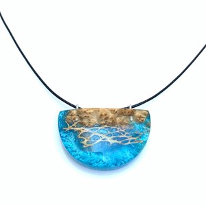 May include: A turquoise and brown resin pendant necklace with a black cord. The pendant is shaped like a half-circle and features a wood grain pattern.