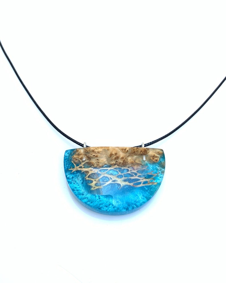 May include: A turquoise and brown resin pendant necklace with a black cord. The pendant is shaped like a half-circle and features a wood grain pattern.