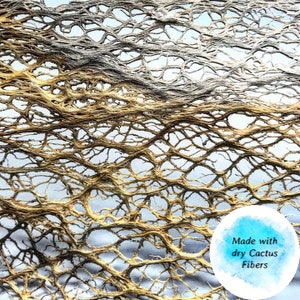 May include: Close-up of a woven material made with dry cactus fibers. The fibers are a light brown color and create a delicate, intricate pattern.