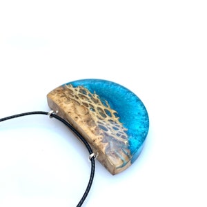 May include: A half-moon shaped pendant necklace with a blue and brown resin design. The pendant is attached to a black cord.