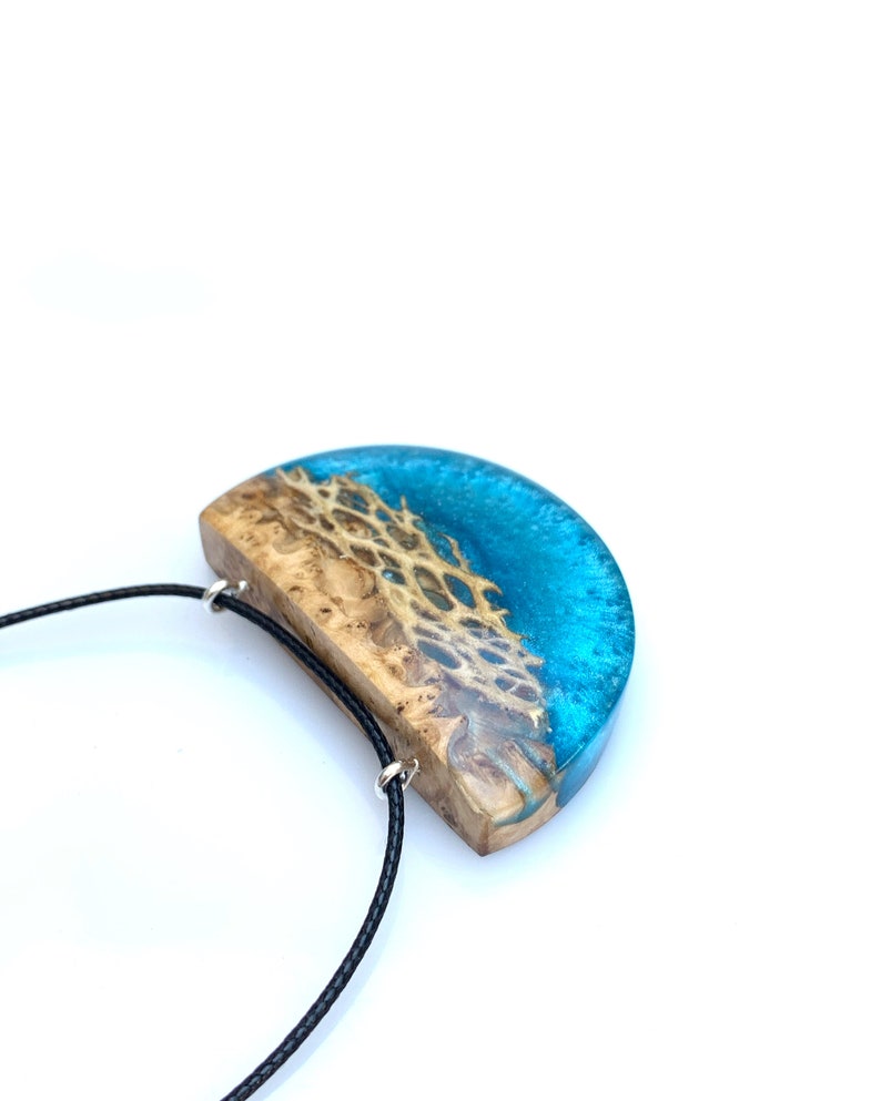 May include: A half-moon shaped pendant necklace with a blue and brown resin design. The pendant is attached to a black cord.