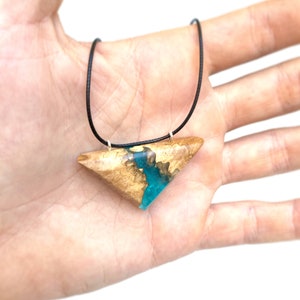 Op de afbeelding: Een ketting met een driehoekige hanger van hout en turquoise hars. De hanger is aan een zwart koord bevestigd.