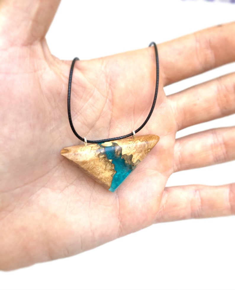 Op de afbeelding: Een ketting met een driehoekige hanger van hout en turquoise hars. De hanger is aan een zwart koord bevestigd.