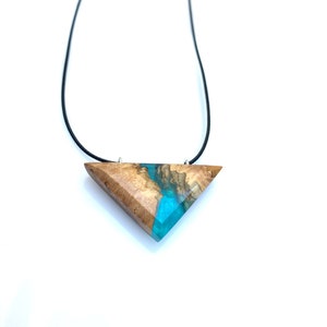 Op de afbeelding: Een ketting met een driehoekige hanger van hout en blauwe hars. De hanger is bevestigd aan een zwart koord.