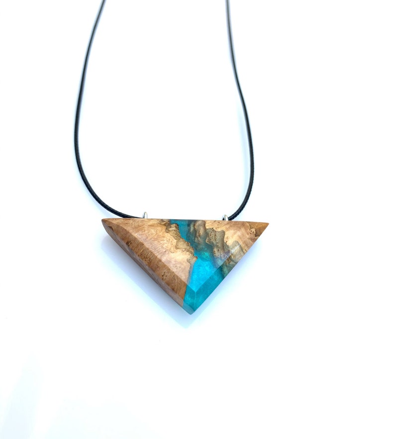 Op de afbeelding: Een ketting met een driehoekige hanger van hout en blauwe hars. De hanger is bevestigd aan een zwart koord.