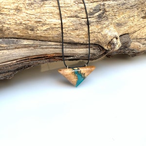 Op de afbeelding: Een ketting met een driehoekige hanger van hout en turquoise hars. De hanger hangt aan een zwart koord.