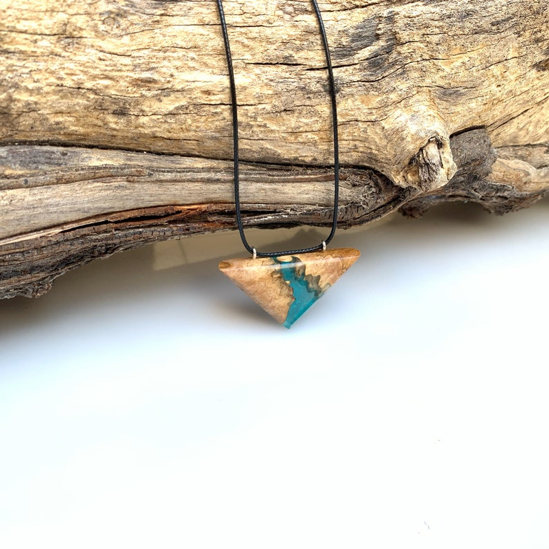 Op de afbeelding: Een ketting met een driehoekige hanger van hout en turquoise hars. De hanger hangt aan een zwart koord.