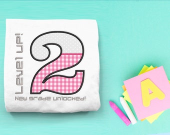 Può includere: Maglietta bianca con un numero 2 a scacchi rosa e bianco e il testo "Level Up! New grade unlocked!"