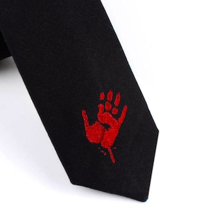 Könnte beinhalten: Schwarze Krawatte mit einem roten Handabdruck-Design. Der Handabdruck ist stilisiert und scheint Blut zu tropfen.