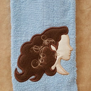 May include: A blue towel with a brown embroidered design of a woman's face with curly hair.