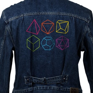 Puede incluir: Una chaqueta vaquera con un diseño geométrico colorido en la espalda. El diseño presenta seis formas diferentes, incluyendo una pirámide, un cubo, un dodecaedro y un tetraedro.