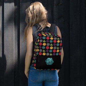 May include: A black backpack with a colorful dice pattern and a large teal d20 dice on the front pocket.