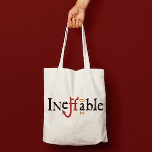 May include: White tote bag with black text that reads "Ineffable" and a red devil with a halo above its head.
