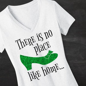 May include: White V-neck t-shirt with the text "THERE IS NO PLACE LIKE HOME..." and a green glitter shoe graphic.