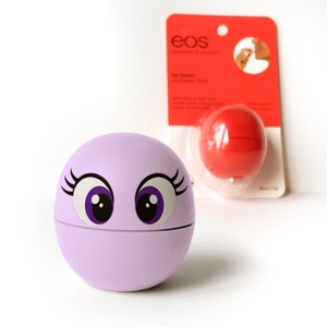 May include: A purple lip balm sphere with a cartoon face featuring large eyes and eyelashes. The lip balm is from the brand EOS, which is written on the packaging.