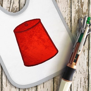 May include: A white bib with a red felt-like fez embroidered on it. A white and silver sonic screwdriver with a green tip is lying next to the bib.