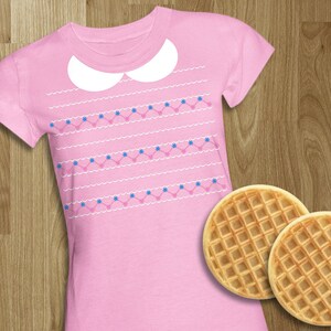 May include: Pink t-shirt with a white Peter Pan collar and a pattern of blue flowers and white waves. Two waffle cookies are in the bottom right corner of the image.